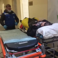 Санитар переносит парализованного пациента с каталки на носилки в машине скорой помощи